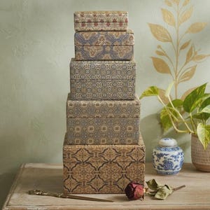 May include: A vertical stack of five rectangular storage boxes with lids, each featuring a distinct geometric pattern in shades of blue, tan, and cream. The boxes are arranged from smallest at the top to largest at the base, creating a tiered tower.