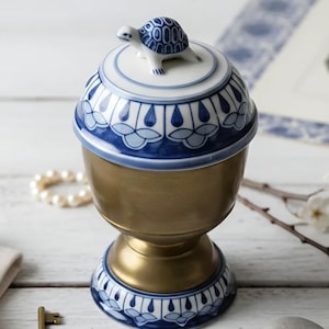 May include: A decorative lidded jar featuring a metallic gold finish on the central body and base. The lid and base are adorned with blue and white floral patterns. A small, sculpted ceramic turtle sits atop the center of the lid.