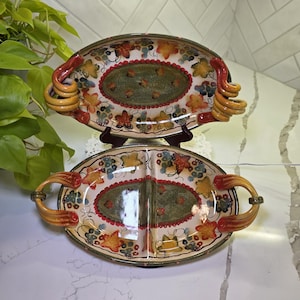 May include: Two oval serving platters with a divided design. The platters feature a colorful grape and leaf motif with red, yellow, and green accents. Each platter has a unique handle design.