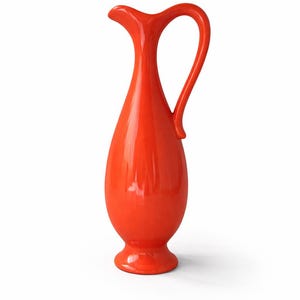 May include: A bright orange ceramic jug with a slender, elongated form and a curved handle. The jug has a small, round base and a spout for pouring. This decorative jug is a stylish addition to any home decor.
