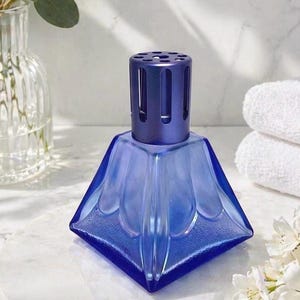 May include: A square-based blue glass fragrance lamp with a textured surface and a matte dark blue metal vented cap. The lamp features a geometric design with raised petal-like panels on each side, tapering toward the top metal burner assembly.