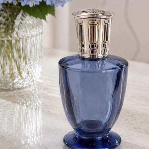 May include: A deep blue glass fragrance lamp with a faceted, tapered body and a wide circular base. The top features a polished silver-toned metal crown with a decorative cut-out pattern, designed to sit securely on the neck of the glass vessel.