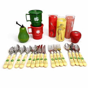 Peut inclure: Ensemble d'articles de cuisine vintage : tasses vertes et rouges, verres à motifs et couverts à manches jaunes. Un bouchon de bouteille vert en forme de poire et une pomme rouge sont également présents.