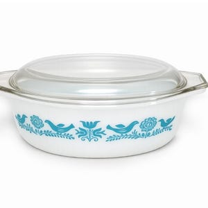 May include: White casserole dish with a clear glass lid. The dish features a turquoise bird and floral pattern around the rim. The dish has two handles and is designed for oven use. The dish is approximately 8 inches in diameter.