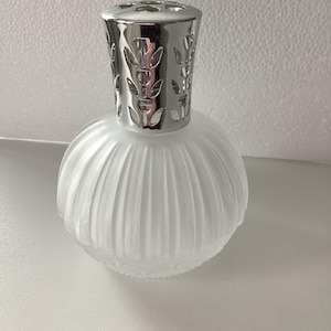Peut inclure: Un diffuseur de parfum en verre dépoli avec un bouchon en métal argenté. Le corps en verre rond et nervuré a une finition douce et mate. Le bouchon présente un motif de feuilles décoratives.
