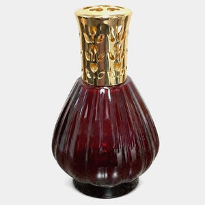 Peut inclure: Une lampe à parfum en verre rouge profond avec un corps bulbeux et nervuré, surmontée d'un capuchon en métal doré brillant doté d'un motif découpé décoratif. La lampe présente une base large qui s'affine vers le haut, créant une silhouette.