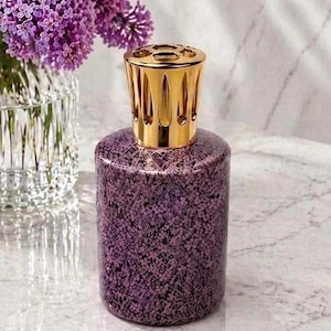 Peut inclure: Une lampe à parfum cylindrique avec une finition en verre craquelé violet et noir et un capuchon couronne en métal doré poli. La lampe présente une base plate et lisse ainsi qu'un couvercle décoratif ajouré pour la diffusion de parfum.