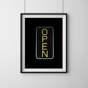 Könnte beinhalten: Gerahmter Druck mit einem gelben Neon-Schild mit der Aufschrift "OPEN" vor schwarzem Hintergrund. Das Schild hat einen türkisfarbenen Rand. Das Kunstwerk hängt an einer weißen Wand.