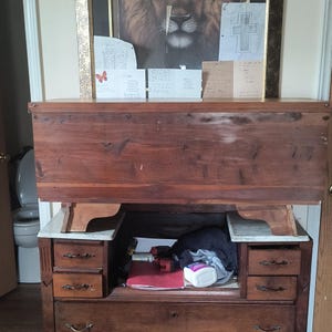 May include: A vintage wooden desk with a dark brown finish. The desk features multiple drawers, a pull-down writing surface, and a storage area. The desk has a classic design with ornate hardware and a warm, inviting aesthetic. The desk is a functional piece of furniture.
