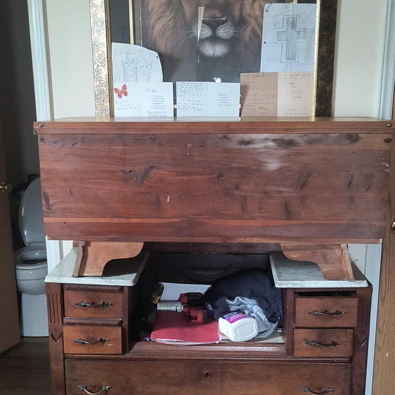 May include: A vintage wooden desk with a dark brown finish. The desk features multiple drawers, a pull-down writing surface, and a storage area. The desk has a classic design with ornate hardware and a warm, inviting aesthetic. The desk is a functional piece of furniture.