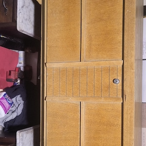 May include: A light-colored wooden cabinet with a keyhole and a series of vertical grooves. The cabinet has a natural wood grain and appears to be part of a larger piece of furniture.
