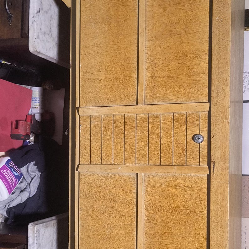 May include: A light-colored wooden cabinet with a keyhole and a series of vertical grooves. The cabinet has a natural wood grain and appears to be part of a larger piece of furniture.