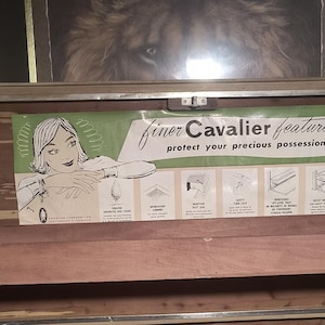 May include: A vintage Cavalier cedar chest with a printed sign featuring a woman and the text "finer Cavalier features protect your precious possessions." The sign highlights features like genuine aromatic red cedar and a safety turn lock.