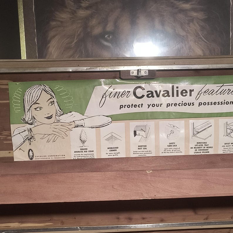 May include: A vintage Cavalier cedar chest with a printed sign featuring a woman and the text "finer Cavalier features protect your precious possessions." The sign highlights features like genuine aromatic red cedar and a safety turn lock.