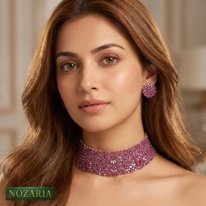 May include: A choker necklace and matching stud earrings featuring a dense arrangement of small, faceted pink stones. The jewellery set displays a uniform, vibrant pink hue throughout, with the brand name NOZARIA printed in the bottom left corner.