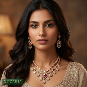 May include: A woman wearing a gold-toned necklace and matching earrings with red and white accents. The necklace has multiple layers with a central pendant. The earrings are dangling. The word "NOZARIA" is at the bottom of the image.