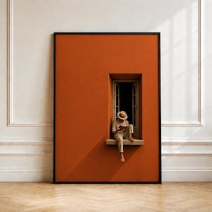 May include: A large rectangular framed wall art piece featuring a solid burnt orange background with a centered window cutout. Inside the window, a figure wearing a straw hat and light-colored clothing sits on the ledge while reading a book.