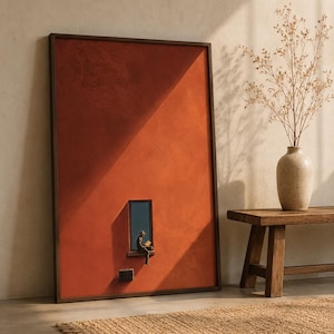Op de afbeelding: Een groot rechthoekig wandkunstwerk met een effen terracotta-kleurige achtergrond. Een klein raam met een donker frame bevindt zich in het onderste gedeelte, met een figuur die op de vensterbank zit en een boek leest in het licht.