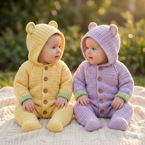 May include: Two babies wearing handmade crochet bear suits. One suit is yellow with green trim, the other is lavender with green trim. Both suits have hoods with bear ears and button closures. The babies are sitting on a cream-colored blanket.