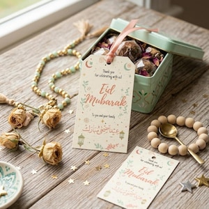 May include: A wooden table displays an Eid Mubarak gift set. The set includes a mint green tin filled with treats, a beaded bracelet with a gold spoon, and decorative tags with the text "Eid Mubarak".