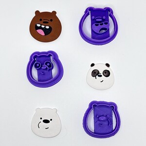 May include: Three purple plastic cookie cutters shaped like bear heads, each paired with a corresponding flat bear face cutout. The cutouts include a brown bear, a white panda with black eye patches, and a plain white bear, all featuring cartoon facial expressions.