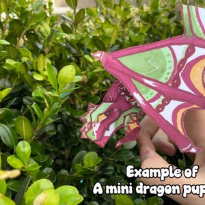 May include: A handmade mini dragon puppet with a red and green color scheme. The dragon's wings and head are visible, with intricate patterns in white, green, and orange. The text "Example of A mini dragon puppet" is at the bottom.