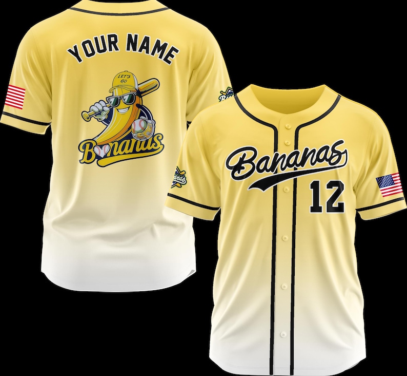 K&ouml;nnte beinhalten: Zwei gelbe Baseball-Trikots. Eines hat "YOUR NAME" auf dem R&uuml;cken und ein Bananen-Maskottchen mit Sonnenbrille und Baseballschl&auml;ger. Das andere Trikot hat "Bananas" und die Nummer "12" auf der Vorderseite. Beide haben schwarze Akzente und amerikanische Flaggen.