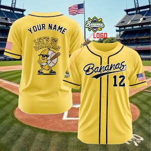 Puede incluir: Camiseta de b&eacute;isbol amarilla con ribete negro, la palabra "Bananas" en cursiva y el n&uacute;mero 12. La camiseta tiene un parche de la bandera estadounidense en la manga. La parte posterior de la camiseta dice "Your Name" y "Let's Go Bananas" con un dibujo de pl&aacute;tano.