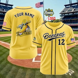 K&ouml;nnte beinhalten: Gelbes Baseball-Trikot mit schwarzem Besatz und dem Wort "Bananas" in Schreibschrift. Die Nummer "12" befindet sich auf der Vorderseite. Auf der R&uuml;ckseite des Trikots stehen die Worte "Your Name" &uuml;ber einer Bananenfigur mit einem Baseballschl&auml;ger. Ein amerikanischer Flaggenaufn&auml;her befindet sich auf dem &Auml;rmel.