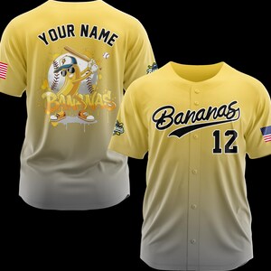 May include: Two yellow baseball jerseys. One features a cartoon banana playing baseball with the text "Bananas" and "Your Name". The other jersey has "Bananas" and the number "12" on the front, with an American flag patch.