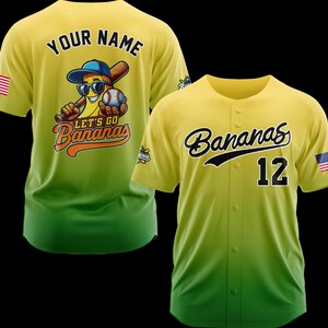 Puede incluir: Dos camisetas de b&eacute;isbol amarillas y verdes. Una camiseta tiene "YOUR NAME" en la espalda y un pl&aacute;tano de dibujos animados con gafas de sol sosteniendo un bate y una pelota de b&eacute;isbol. La otra camiseta tiene "Bananas" y el n&uacute;mero "12" en la parte delantera.