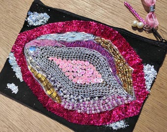 Nécessaire para cosméticos com detalhes em miçangas em formato de vulva.