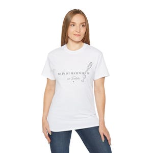 Könnte beinhalten: Weißes T-Shirt mit dem deutschen Text "WEIN IST AUCH NUR TEE mit Tralala" und einer Grafik von Weinflasche und Glas. Ein lässiges Kleidungsstück für den Alltag.