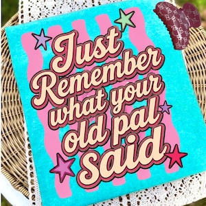 Peut inclure: Un t-shirt turquoise vif avec un motif de rayures verticales ondulées roses et le texte Just Remember what your old pal Said dans une police rétro marron et crème, agrémenté de petites étoiles violettes, roses et vertes, avec une pince à cheveux marron.