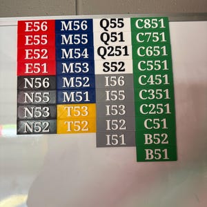 May include: A series of rectangular labels in various colours, each displaying a unique combination of letters and numbers. The labels are arranged in a grid-like pattern. Colours include red, blue, black, white, grey, yellow, and green. The text is in a sans-serif font.