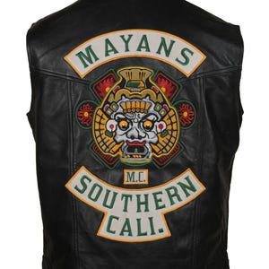 May include: Black leather vest with a large embroidered patch on the back. The patch features the text "MAYANS" above a detailed Mayan-inspired design and "SOUTHERN CALI" below. The vest has a classic biker style.