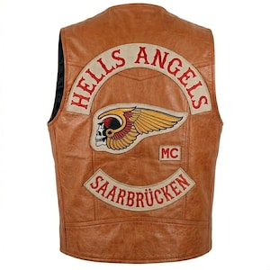 Puede incluir: Un chaleco de cuero marrón con el logo de "Hells Angels" en la espalda. El logo presenta una calavera alada y el texto "SAARBRÜCKEN". El chaleco tiene un estilo motero clásico.