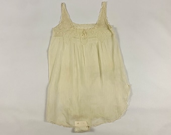 May include: Cream-colored vintage bodysuit with lace trim. The top features a square neckline and delicate lace detailing across the chest and straps. The bottom portion is a brief style with a lace hem.