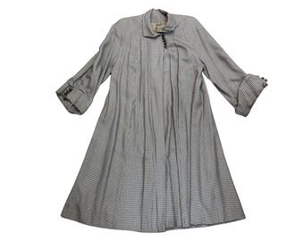 May include: A vintage, long-sleeved coat in a black and white checkered pattern. The coat features a collar, button details on the sleeves, and a flared skirt. The fabric appears to be a lightweight material.