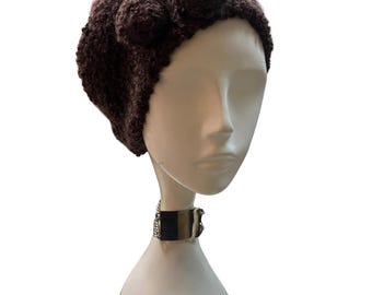 May include: A dark brown knitted hat with a textured appearance. The hat features a rounded shape with three decorative elements on the side. The hat is displayed on a mannequin head with a silver and black choker.