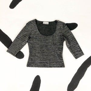 May include: A black and silver striped, three-quarter sleeve top with a scoop neck. The top has a small white label with the text "David Delamare" on the front.