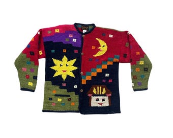 May include: A colorful, button-down cardigan sweater with a whimsical design. The sweater features a large yellow star, a crescent moon, and a house motif. The sleeves and body are adorned with various geometric shapes in red, green, purple, and black.