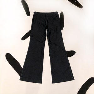 May include: Dark navy blue flared pants with white stitching details. The pants have a zipper closure and a classic, wide-leg design. The fabric appears to be a medium-weight material, suitable for various occasions. The pants are laid flat, showcasing their shape and construction.