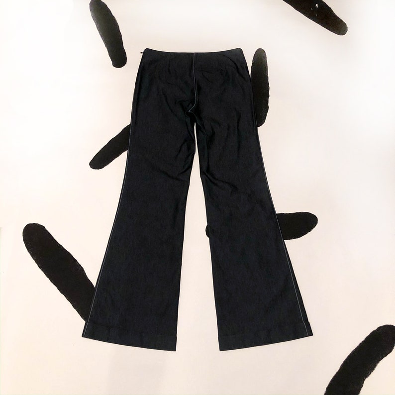 May include: Dark navy blue flared pants with white stitching details. The pants have a zipper closure and a classic, wide-leg design. The fabric appears to be a medium-weight material, suitable for various occasions. The pants are laid flat, showcasing their shape and construction.
