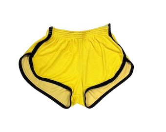 May include: Bright yellow athletic shorts featuring a high-cut leg design with contrasting black trim along the curved hems and side seams. The garment includes an elasticized waistband for a secure fit and a lightweight, textured fabric construction.