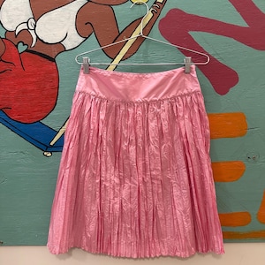 May include: A pink pleated skirt with a high waist and a slightly flared hem.