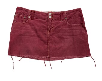 May include: A burgundy corduroy mini skirt with a frayed hem. The skirt has a classic five-pocket design, a button and zipper closure, and belt loops. The fabric has vertical ridges.