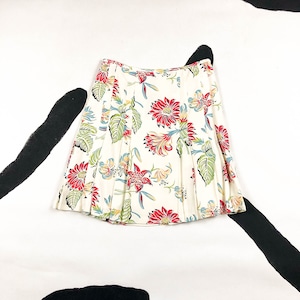 May include: A pleated skirt with a floral pattern. The skirt features a cream-colored background with a vibrant print of red, green, and yellow flowers and leaves. The skirt has a classic A-line shape.
