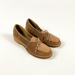 May include: A pair of brown suede shoes with a lace-up design and orange tassels. The shoes have a chunky heel and a rounded toe.
