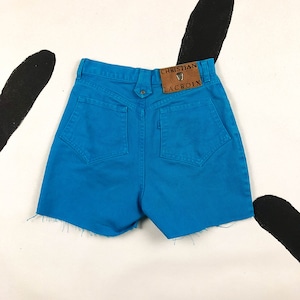 Puede incluir: Pantalones cortos vaqueros de color turquesa brillante con dobladillo sin rematar. Los pantalones cortos tienen dos bolsillos traseros y un parche de cuero con el texto "CHRISTIAN LACROIX". Un artículo de moda vintage.